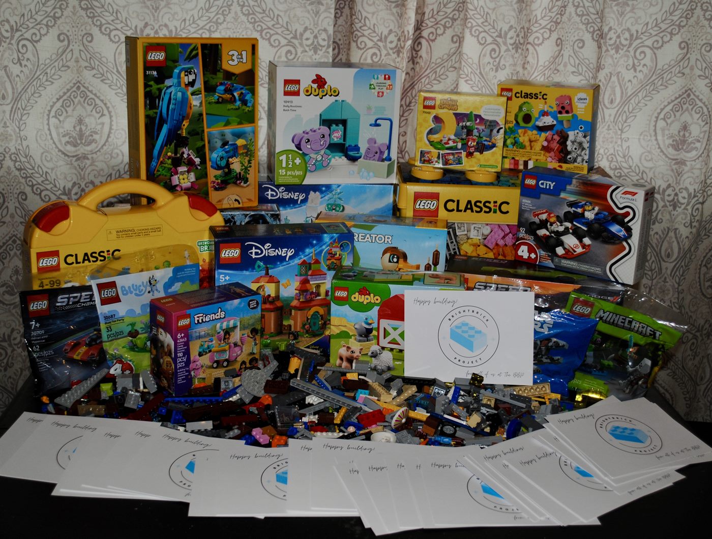 A large donation of new LEGO sets — Duplo, Disney, Classic, City, Friends and more — with a stack of BrightBrick 'Happy building' cards.