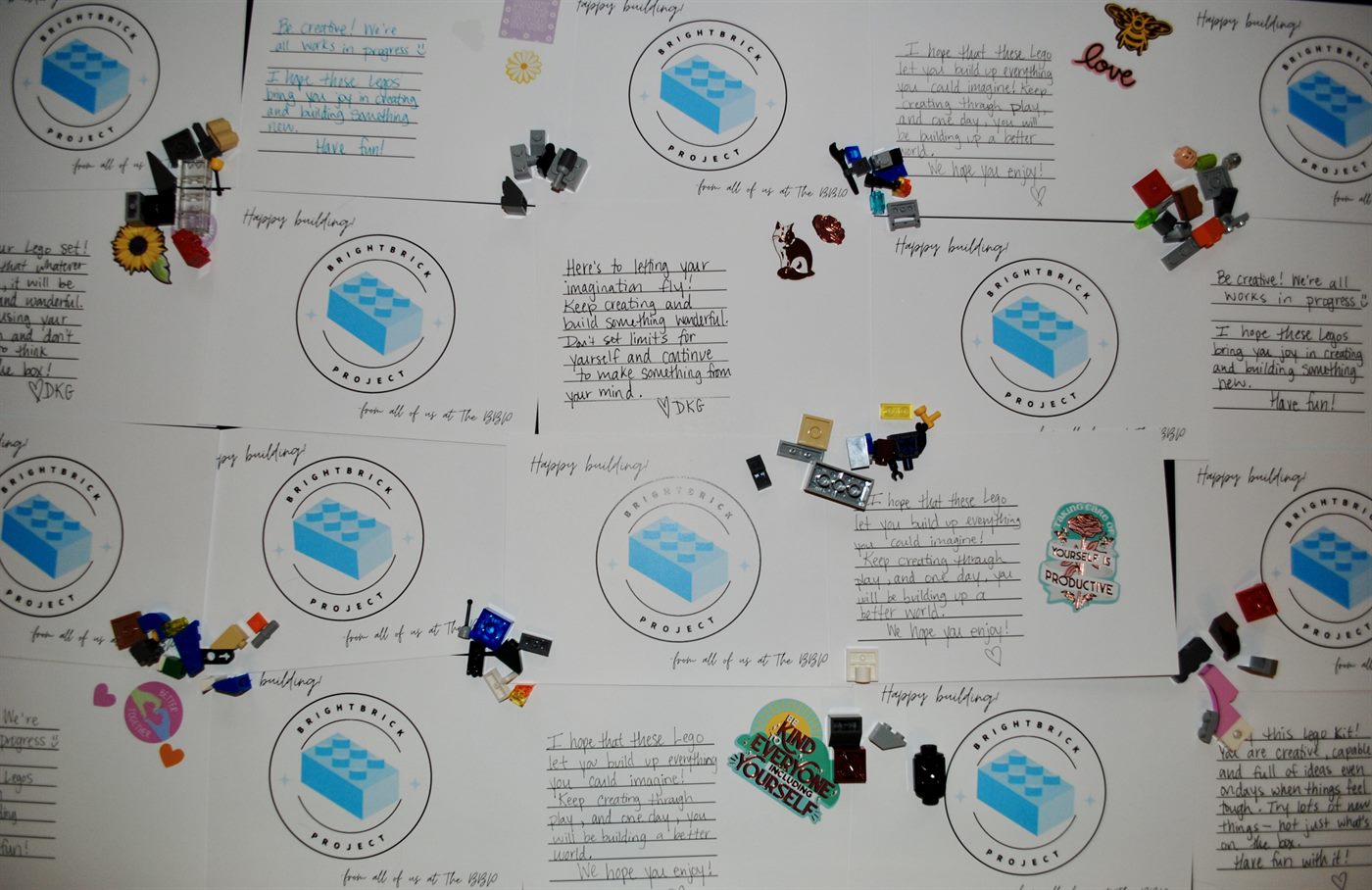 Handwritten 'Happy building' encouragement cards from The BrightBrick Project, surrounded by LEGO pieces and stickers.